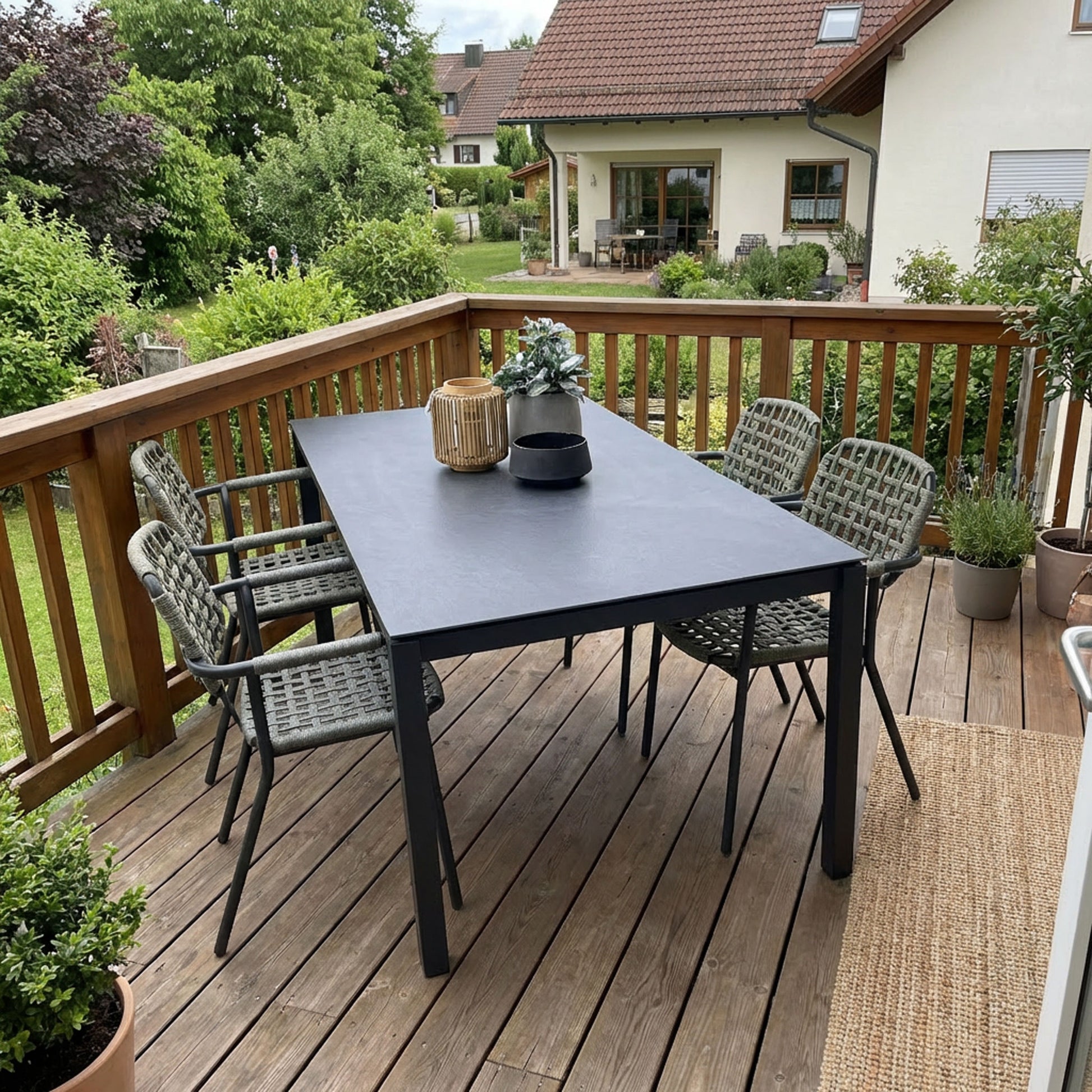schwarzer Gartentisch mit grünen Flechtstühlen auf Balkon